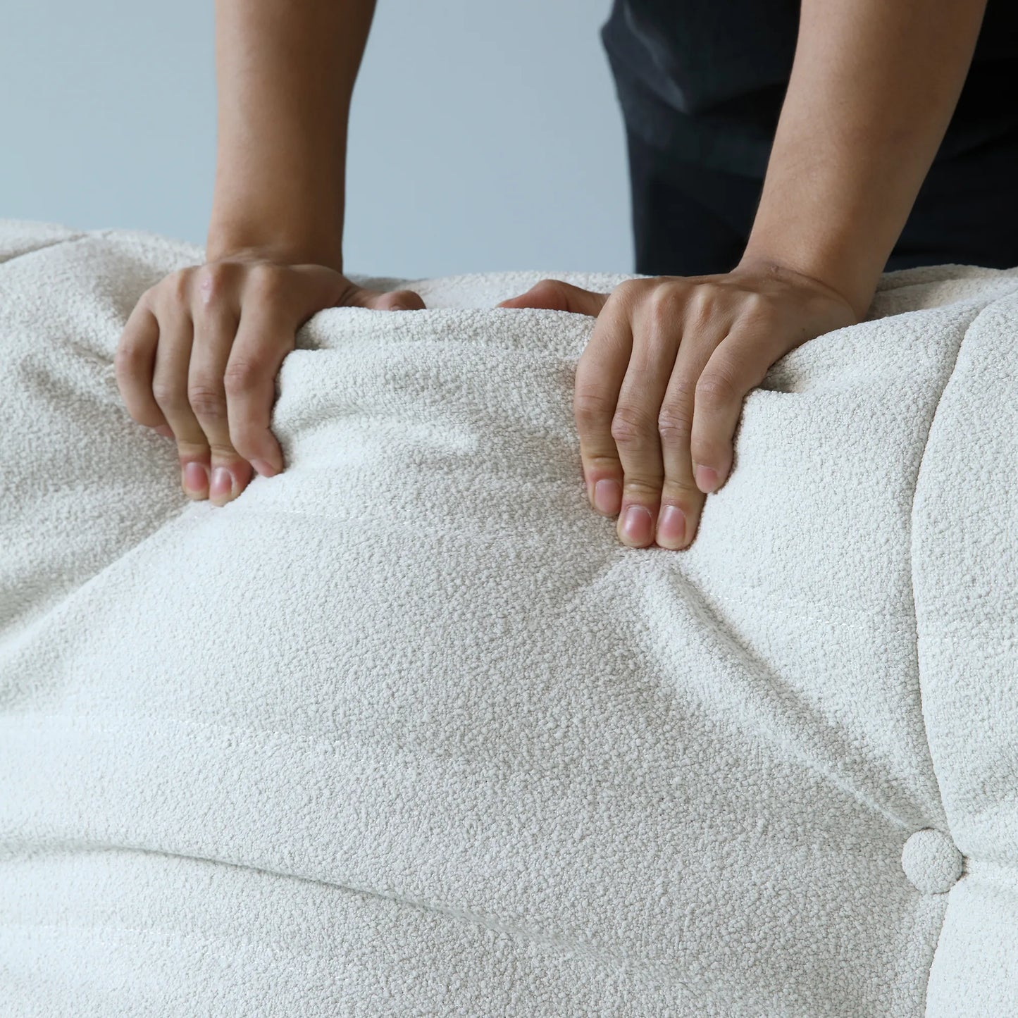 Person pressing on the back cushion of a white sofa to show its softness