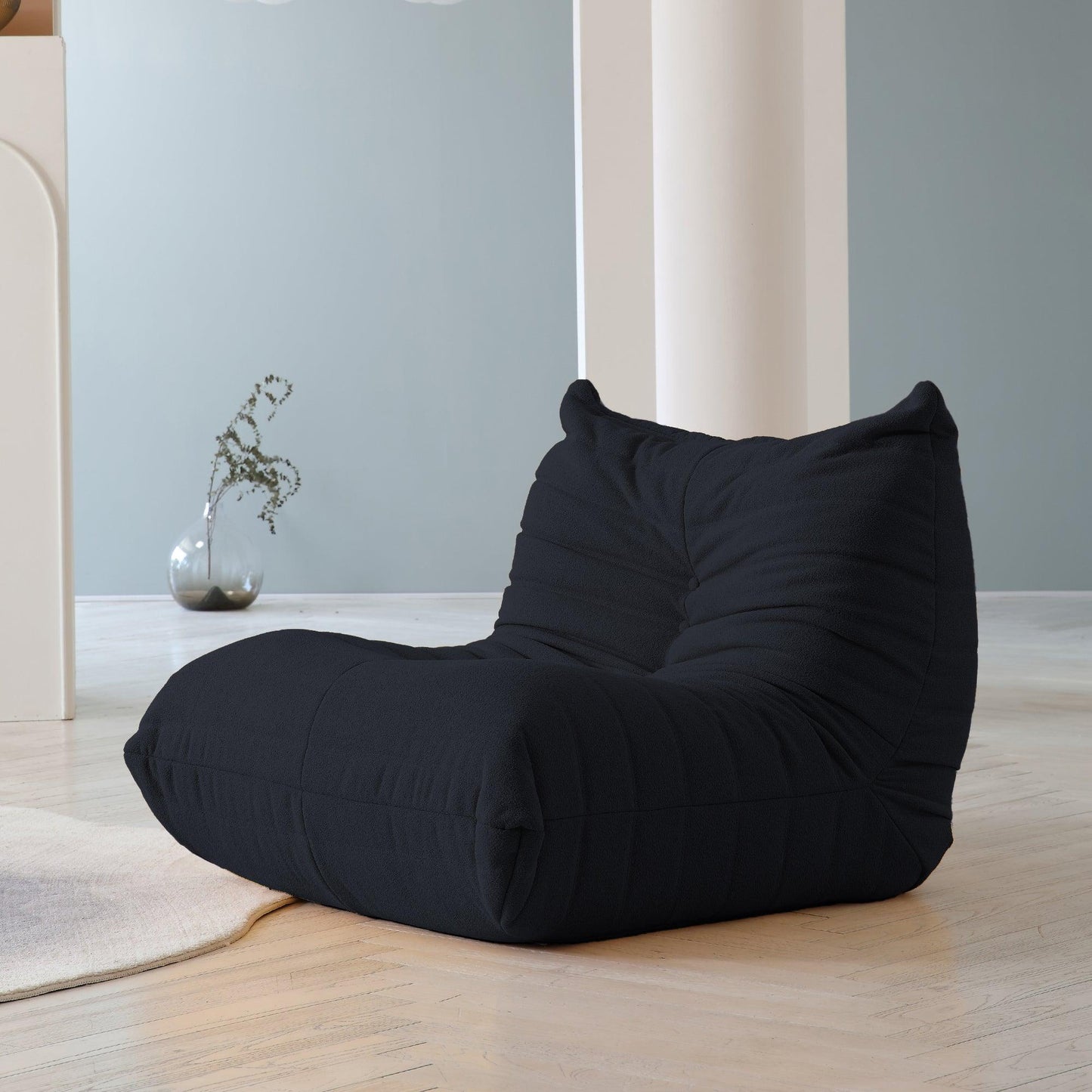 A distinctive black caterpillar-shaped floor armchair placed on a wooden floor in a room with light blue walls.