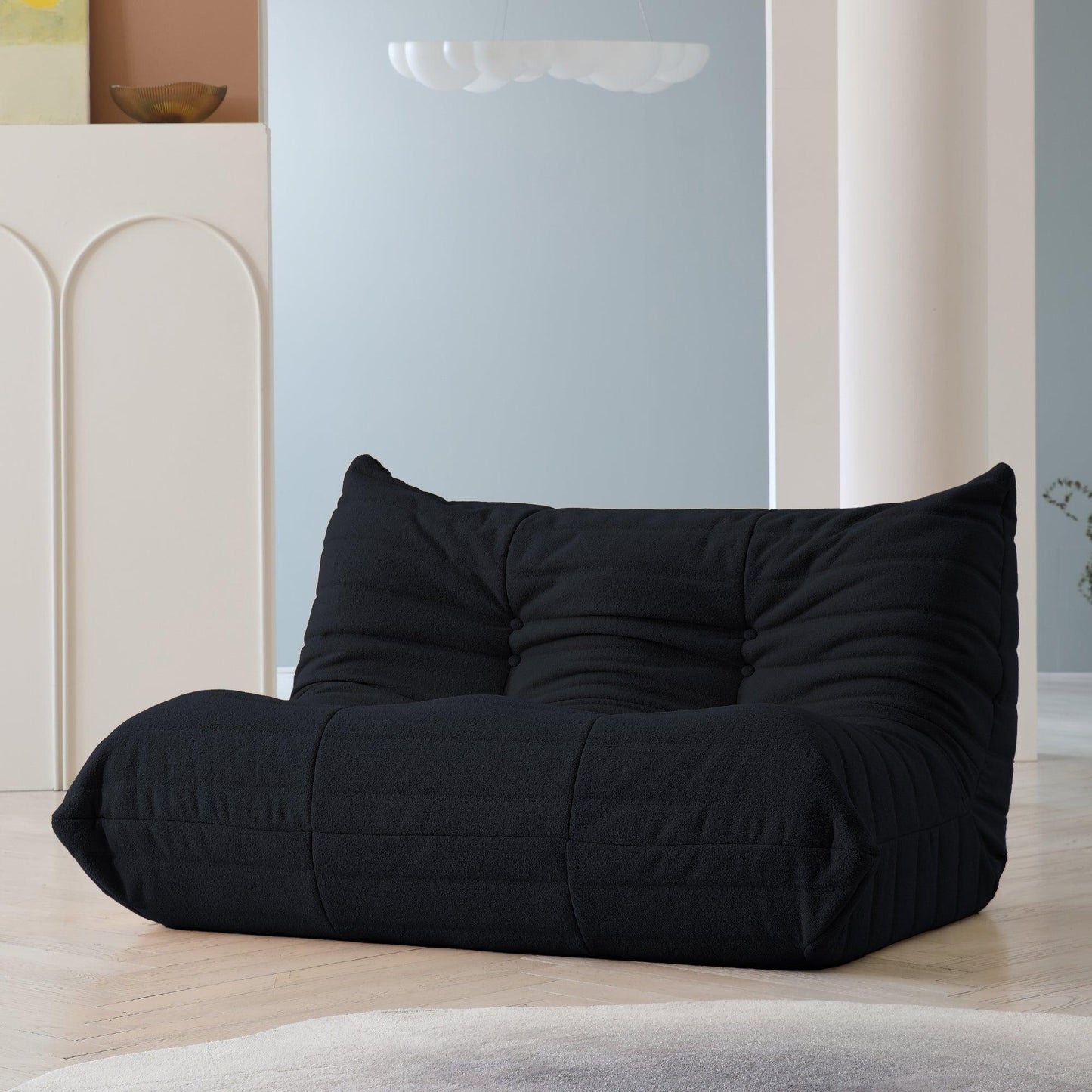 A black, caterpillar-shaped Togo sofa on a wooden floor with light blue wall behind