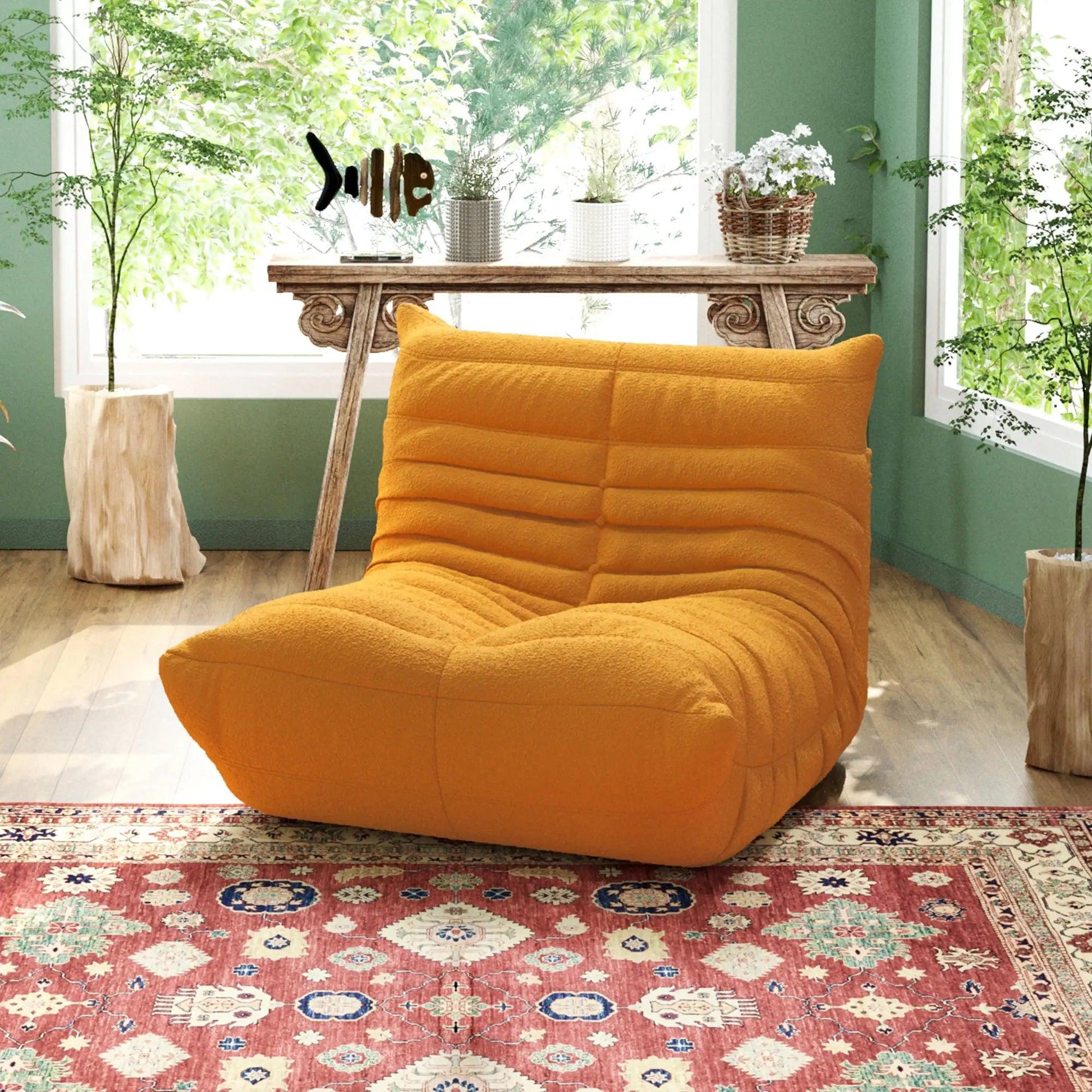 A distinctive yellow caterpillar-shaped floor sofa placed on a patterned rug in a room with green walls and a wooden table.