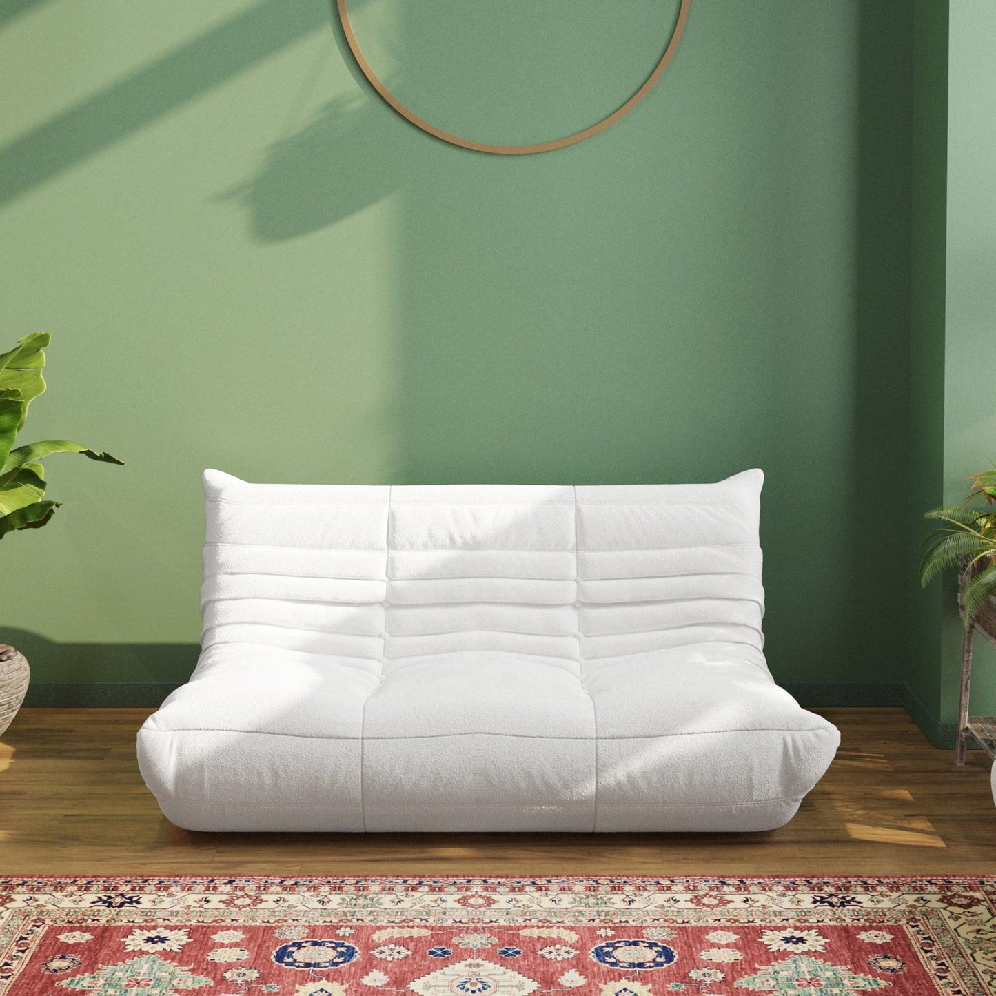A white, caterpillar-shaped Togo sofa on a patterned rug with a green wall in the background.