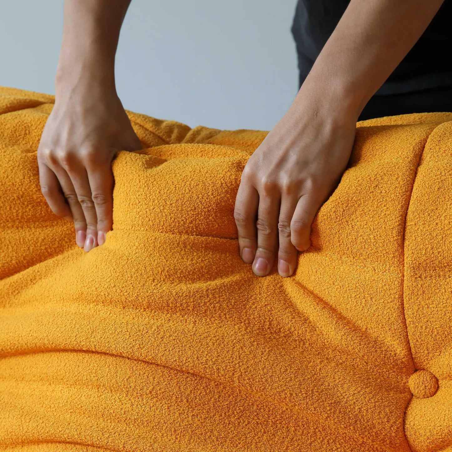Person pressing on the back of an orange togo sofa to show its softness