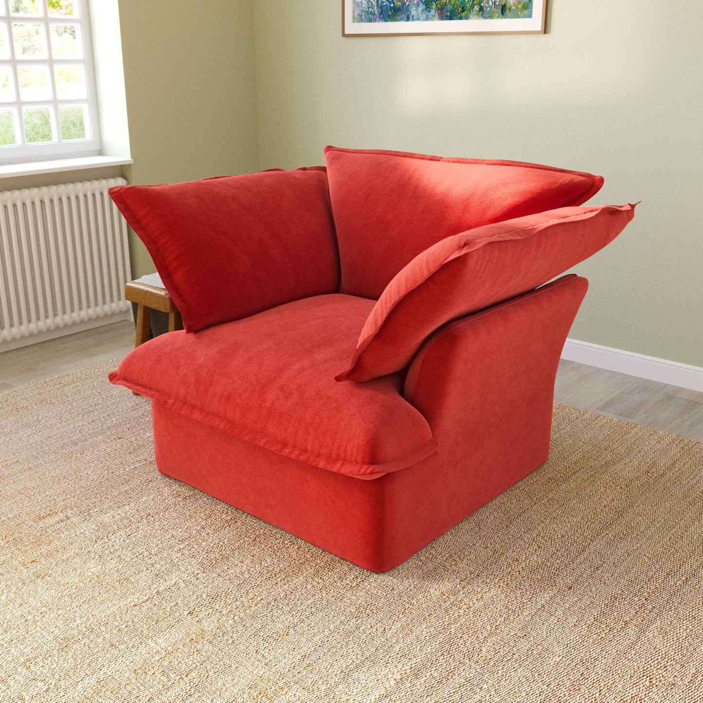 A red velvet accent chair with a cushioned backrest and seat, placed in a room with a light green wall and a framed picture on the wall.