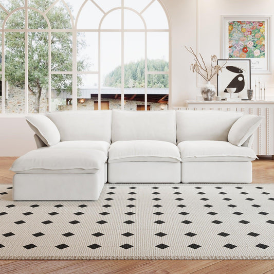 A white L-shaped linen sectional sofa with a storage ottoman positioned in a bright room with large windows, alongside a patterned rug and in front of a wall with artwork.