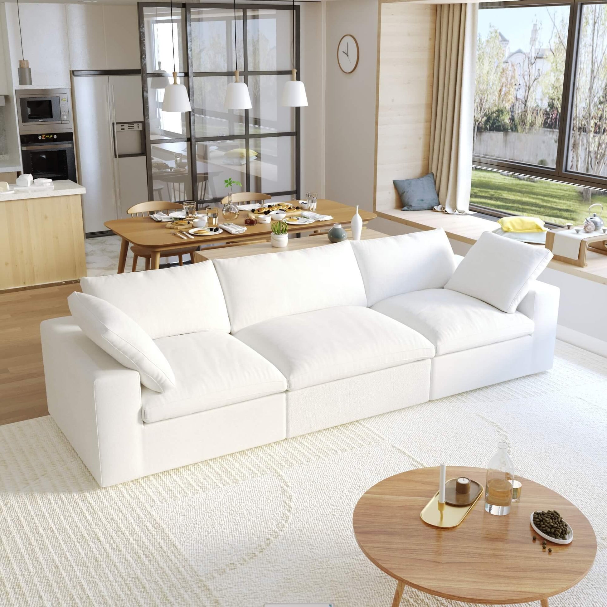 A modern white 3-seater sectional sofa in a living room setting with a round wooden coffee table in front and a kitchen area in the background.