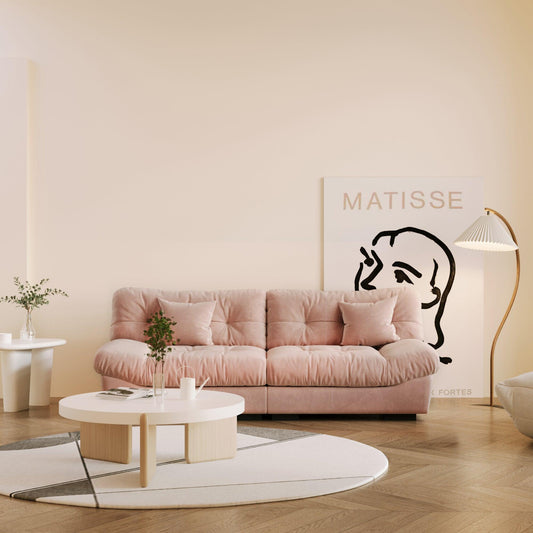 An 89-inch pink microfiber suede sofa with a solid hardwood frame, presented in a warm lightning in a living room setting with minimalistic decor, including a 'Matisse' art print on the wall.