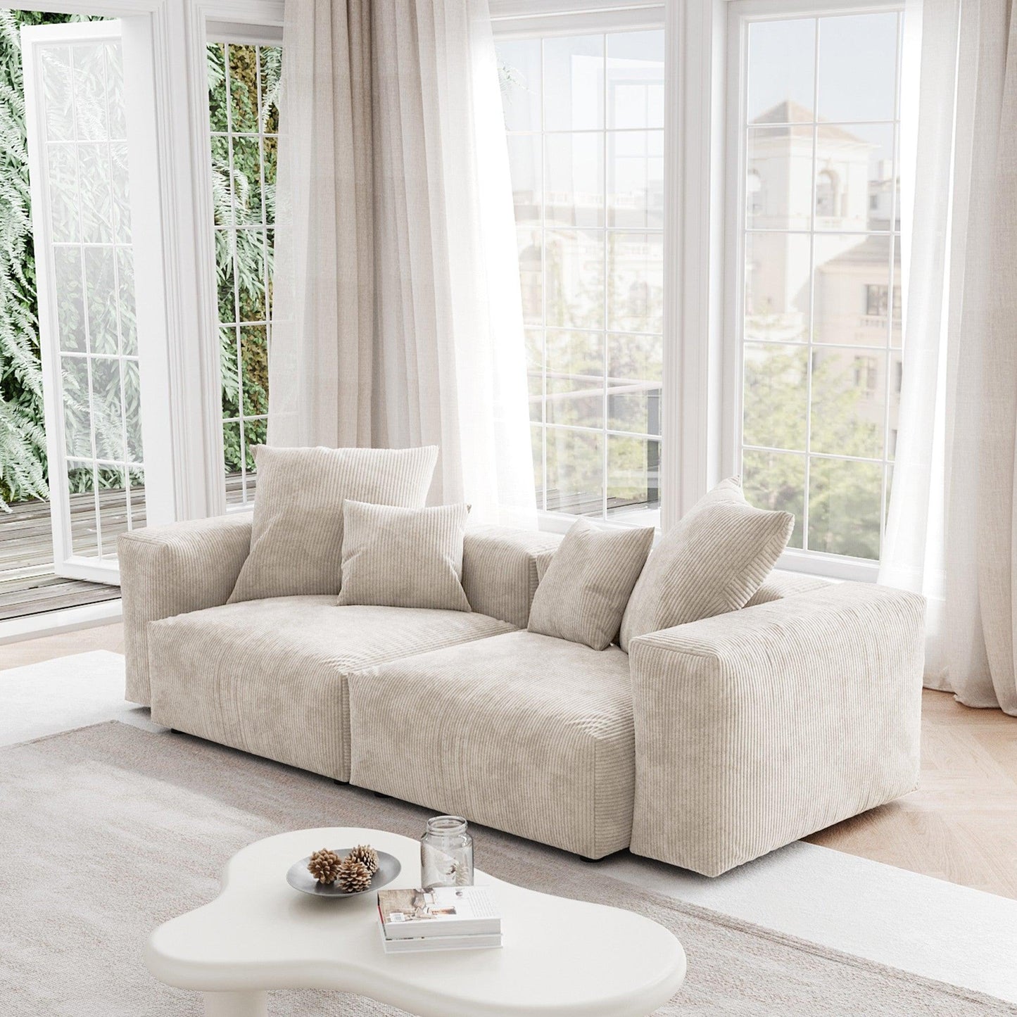 A beige corduroy sectional loveseat sofa with detachable armrests and removable covers, positioned in a bright room with large windows.