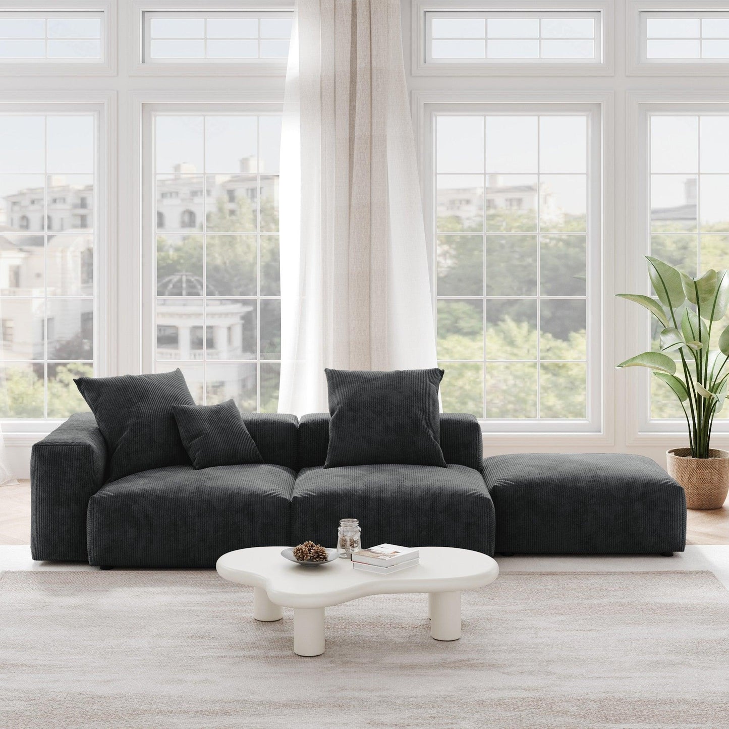A black corduroy sectional lounger sofa with detachable armrests and removable covers, positioned in a bright room with large windows.