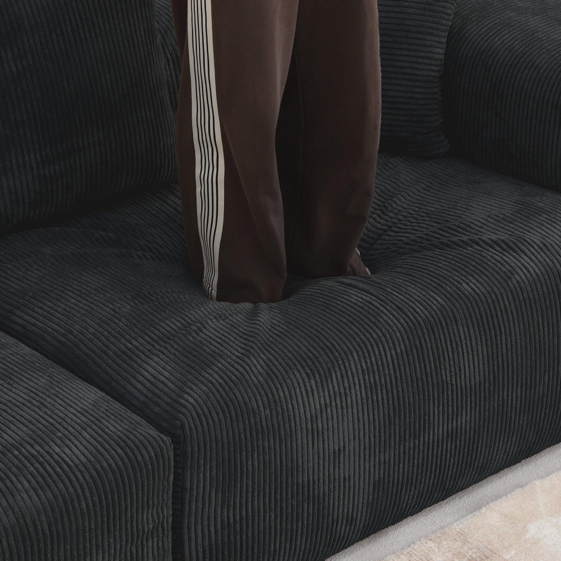 Person standing on a seat cushion of a black corduroy sofa