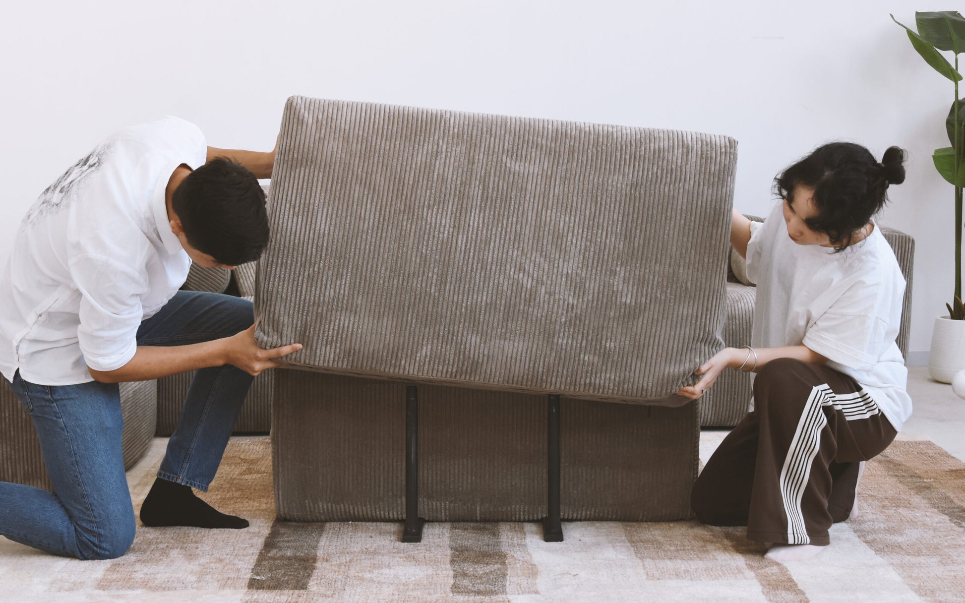 Two people assembling brown corduroy sofa