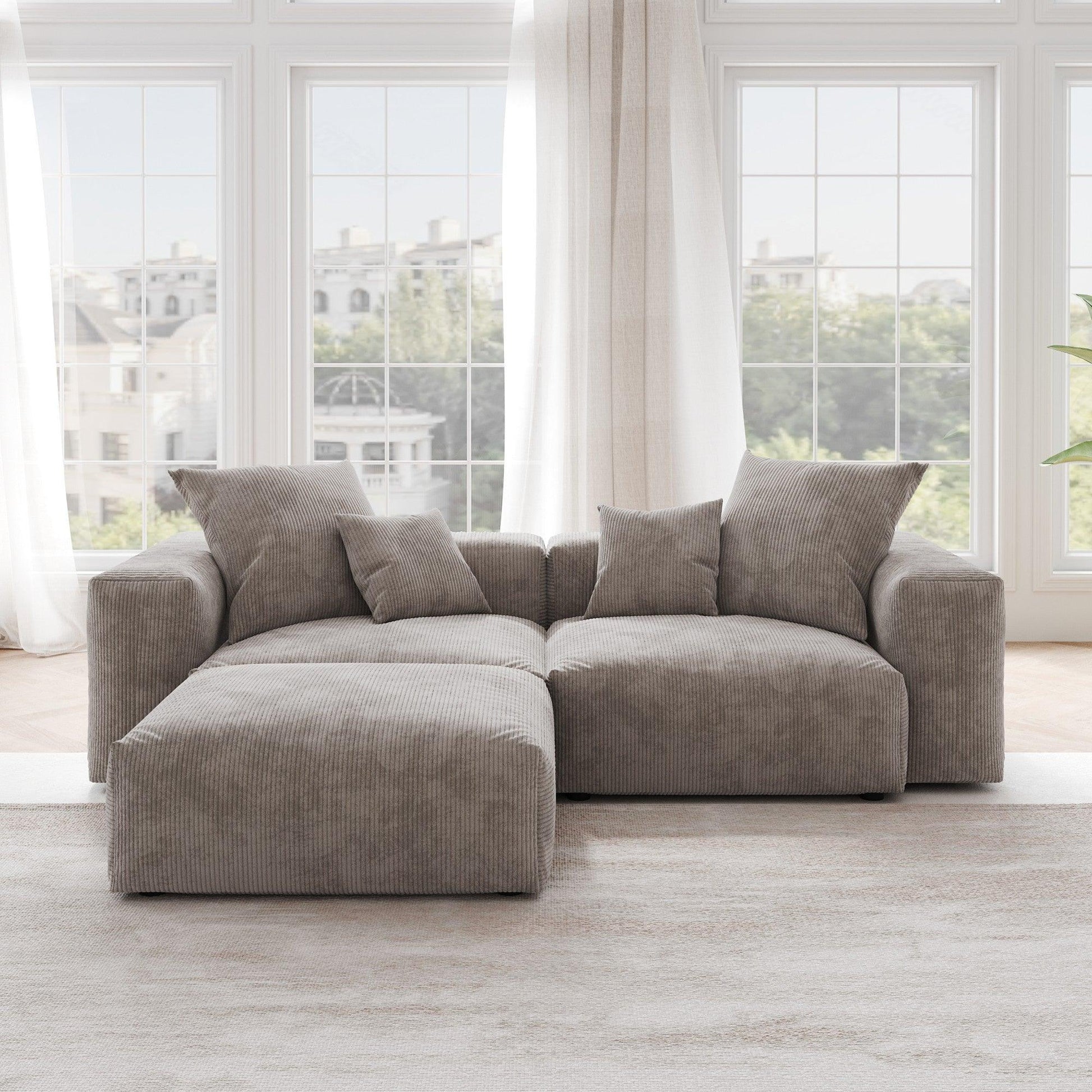 A brown corduroy sectional loveseat sofa with ottoman, detachable armrests, and removable covers, featuring a chaise lounge configuration placed in a room with large windows.