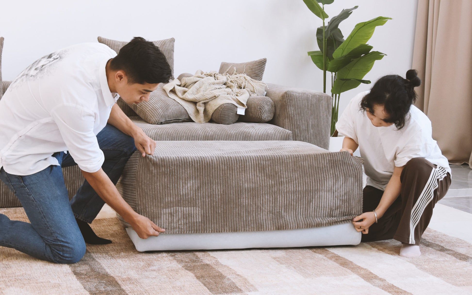Two people putting brown corduroy cover on a sofa frame