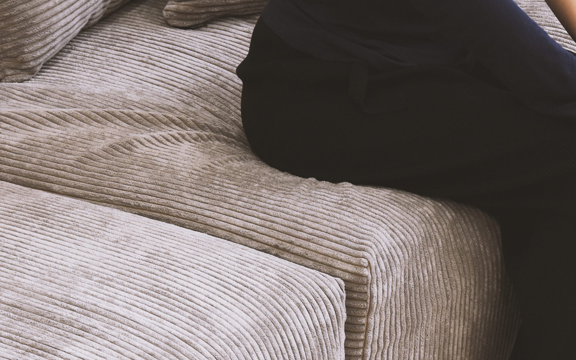 Close-up of a person sitting on a seat cushion of a brown corduroy sofa