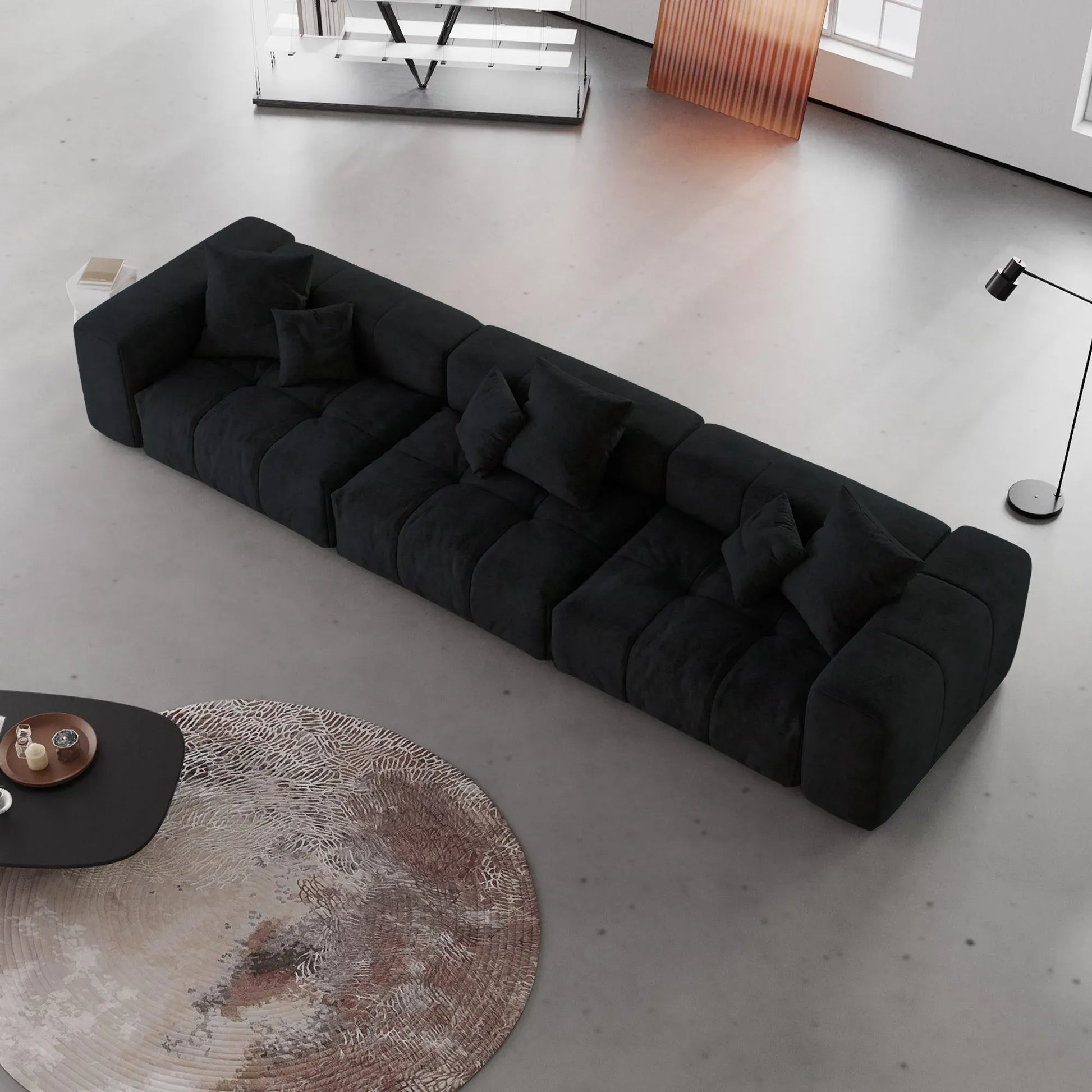 Black 3-seater sofa in a modern living room with a concrete floor and minimal decor.