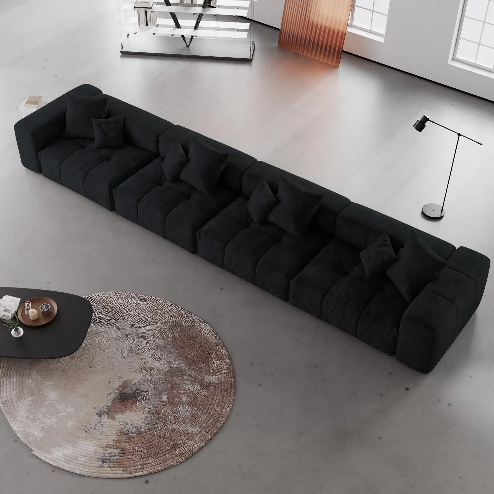 Modern black 4-seater sofa in a minimalistic living room with a round rug and coffee table.