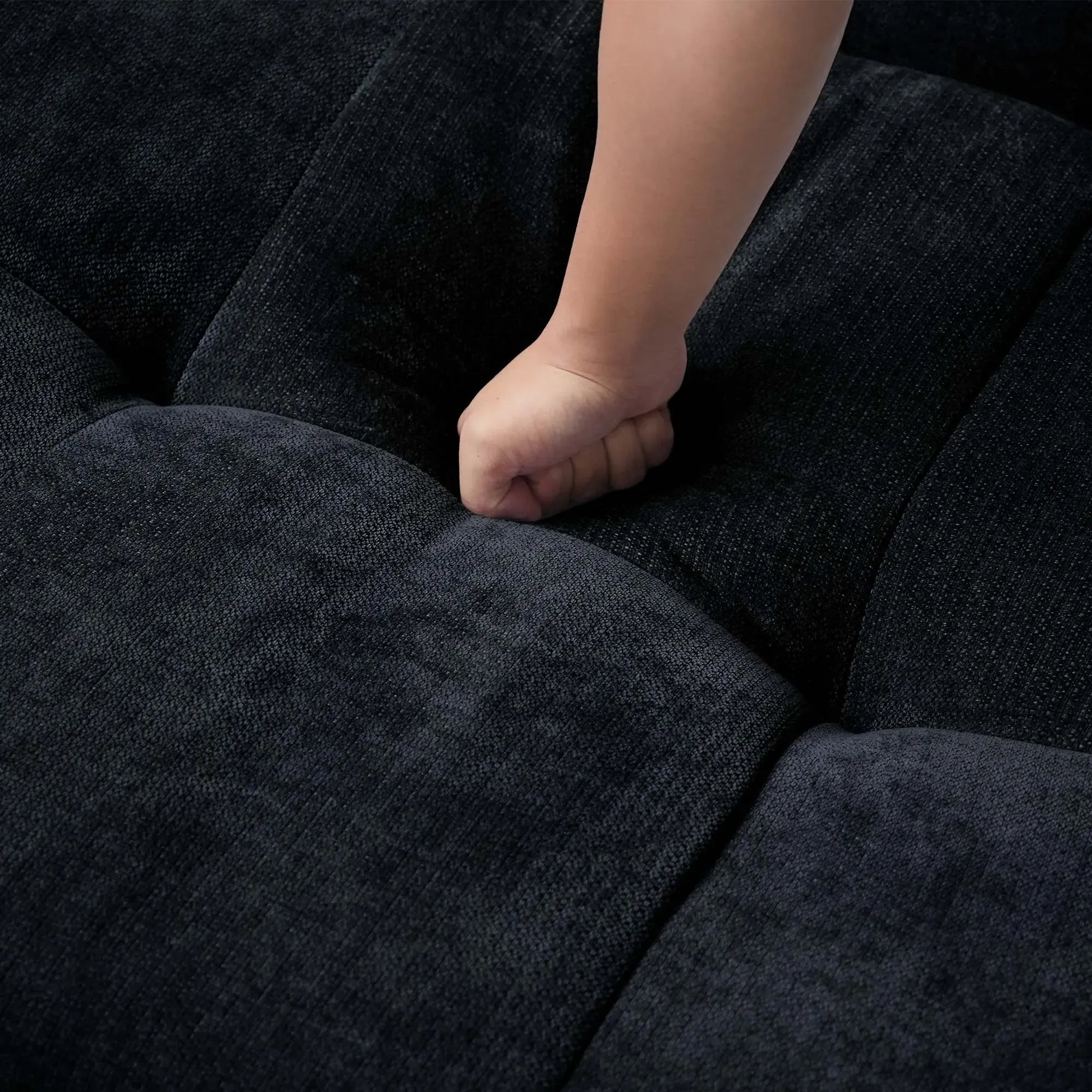 Close-up of a hand pressing on a seat cushion of a black sofa