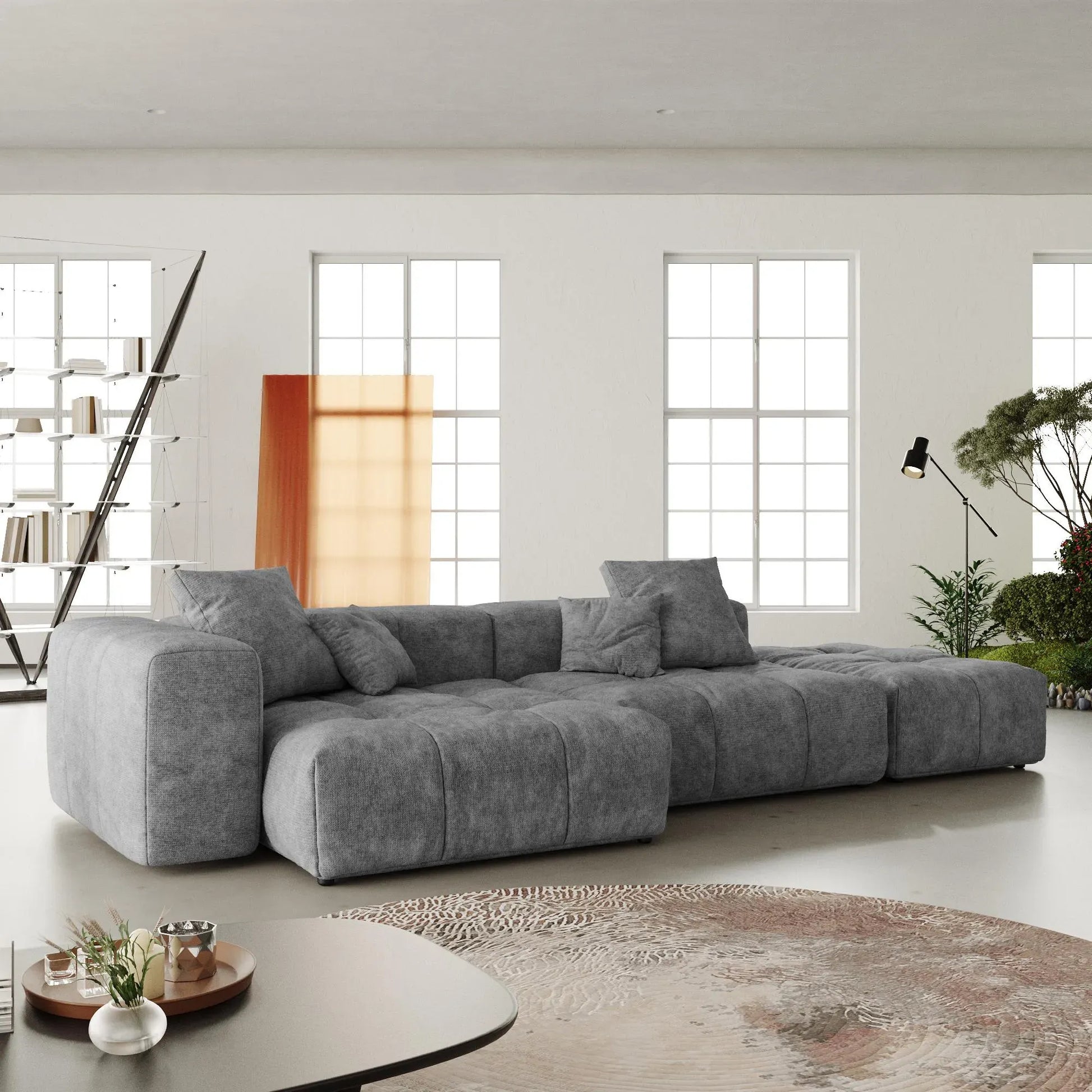 Gray sectional 3-seat lounger sofa in a modern living room with large windows and minimal decor.