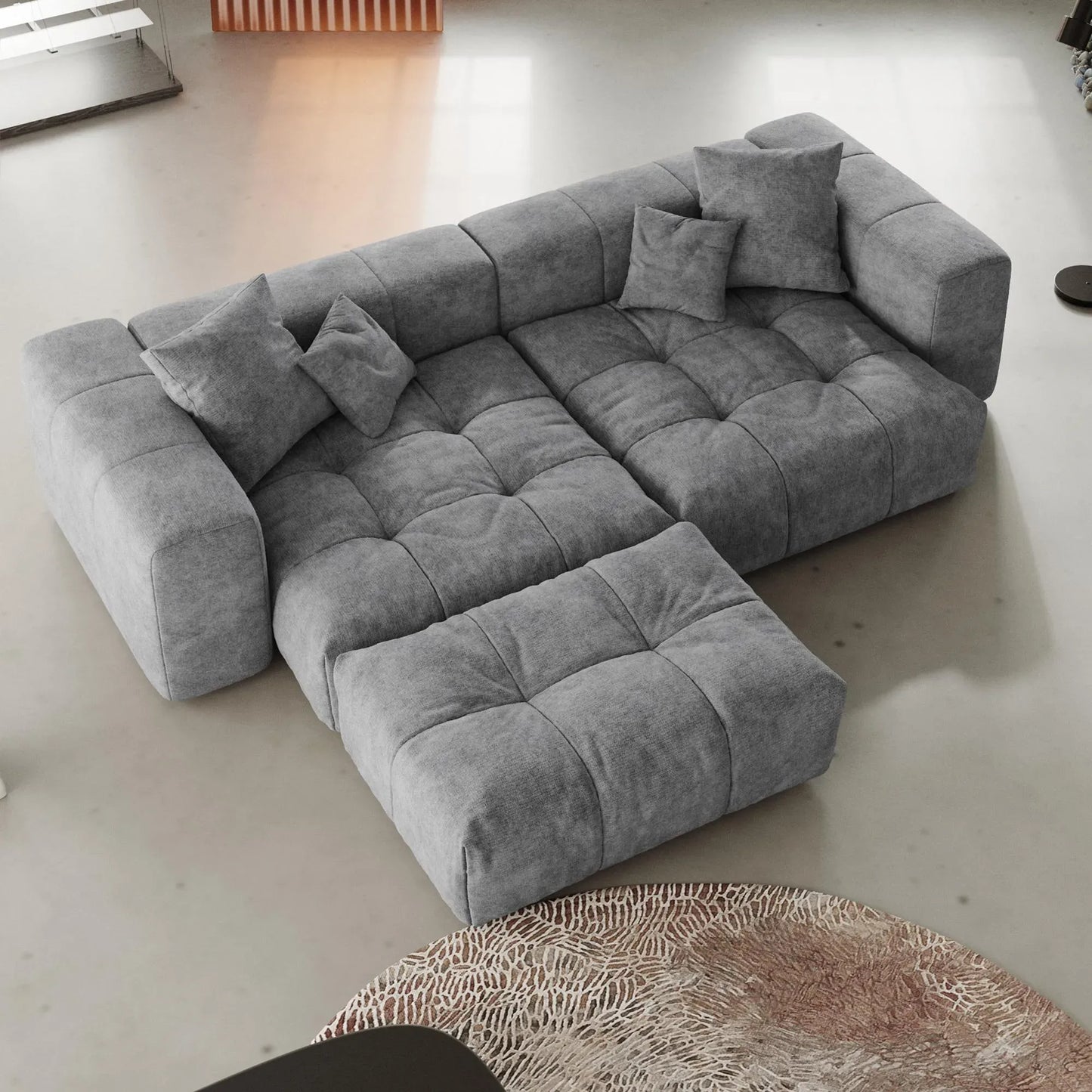 Gray sectional loveseat sofa with ottoman in a minimalistic room with a rug.