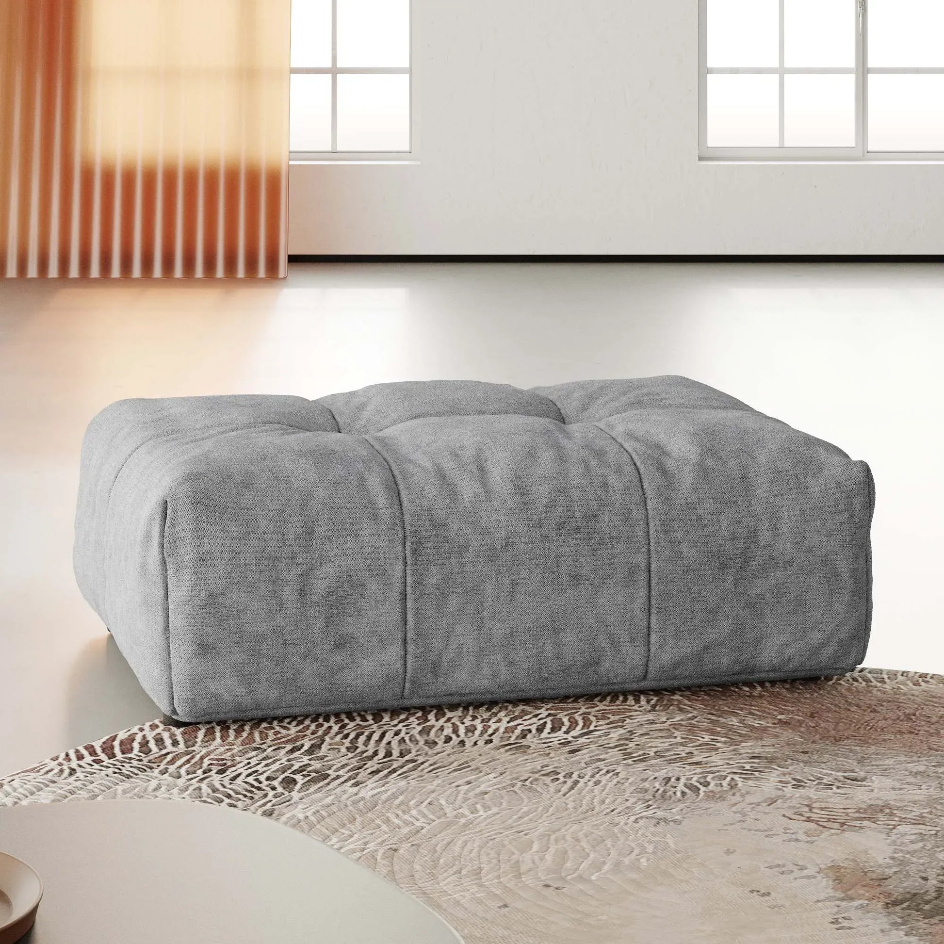Gray upholstered ottoman on a textured rug with a neutral background