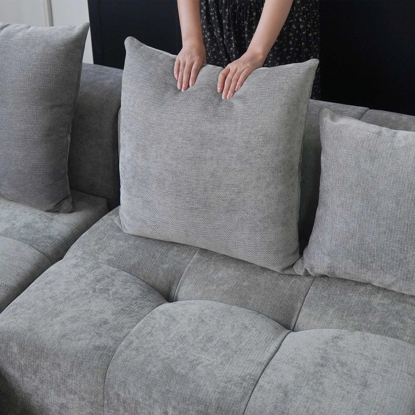 Person adjusting a gray pillow on a gray sofa