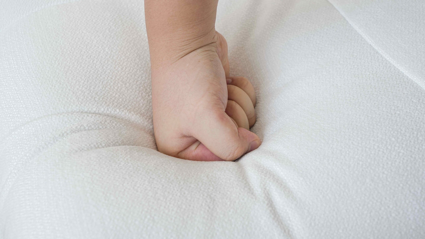A close-up a hand pressing on a white sofa, showcasing its foam density