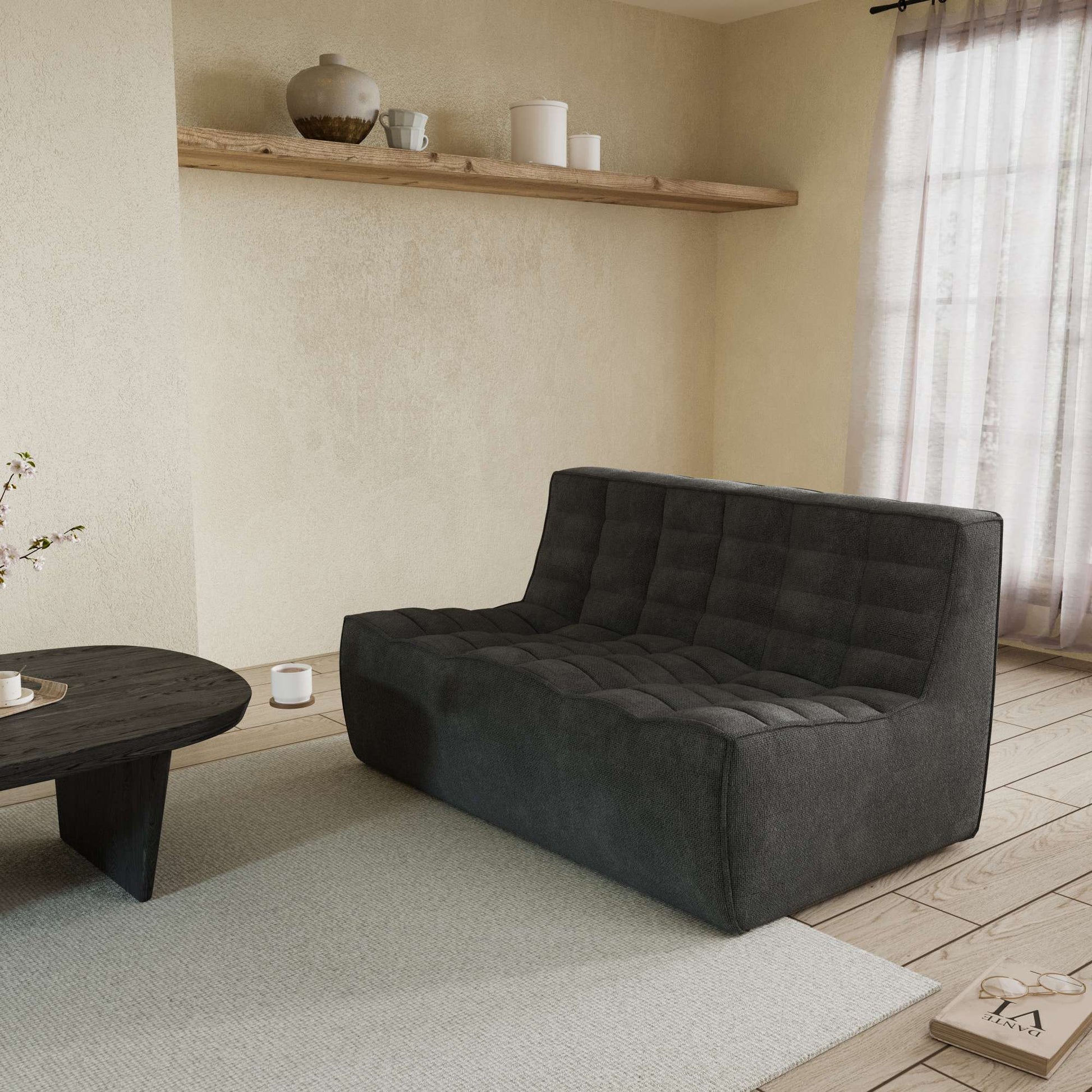 A black Floor Chenille Sofa with an ergonomic caterpillar design, placed in a room with a window, curtains, a small round table, and a book on the floor.