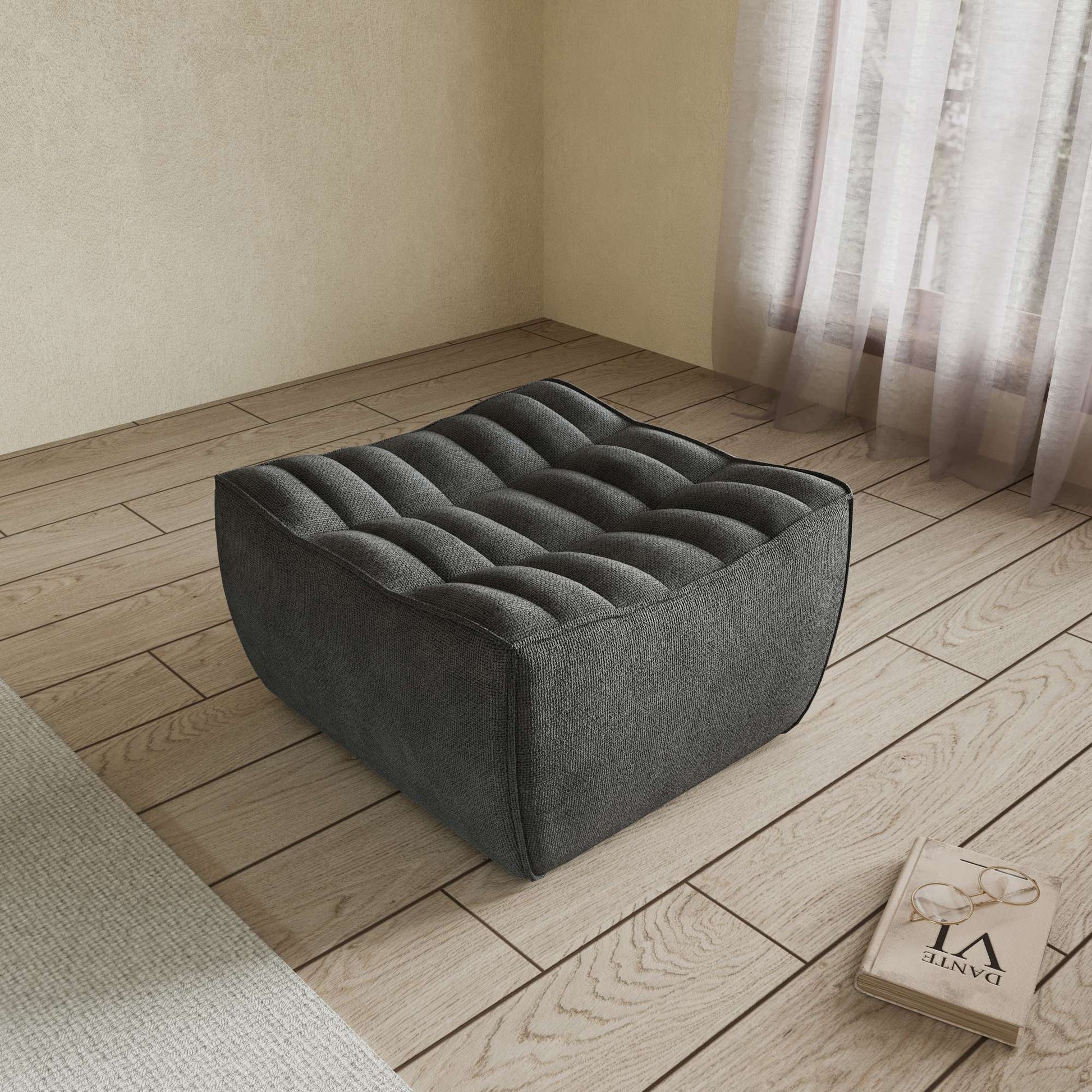 A black chenille ottoman with a minimalist design, placed on a wooden floor with a large window in the background.