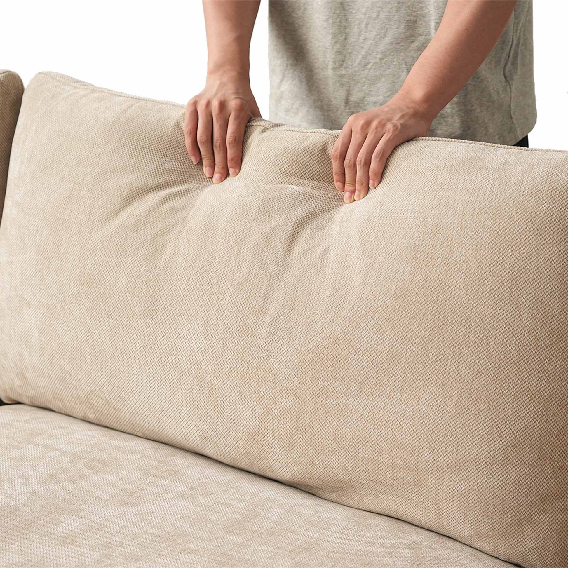 Person squishing a backrest cushion of a khaki sofa to show its softness