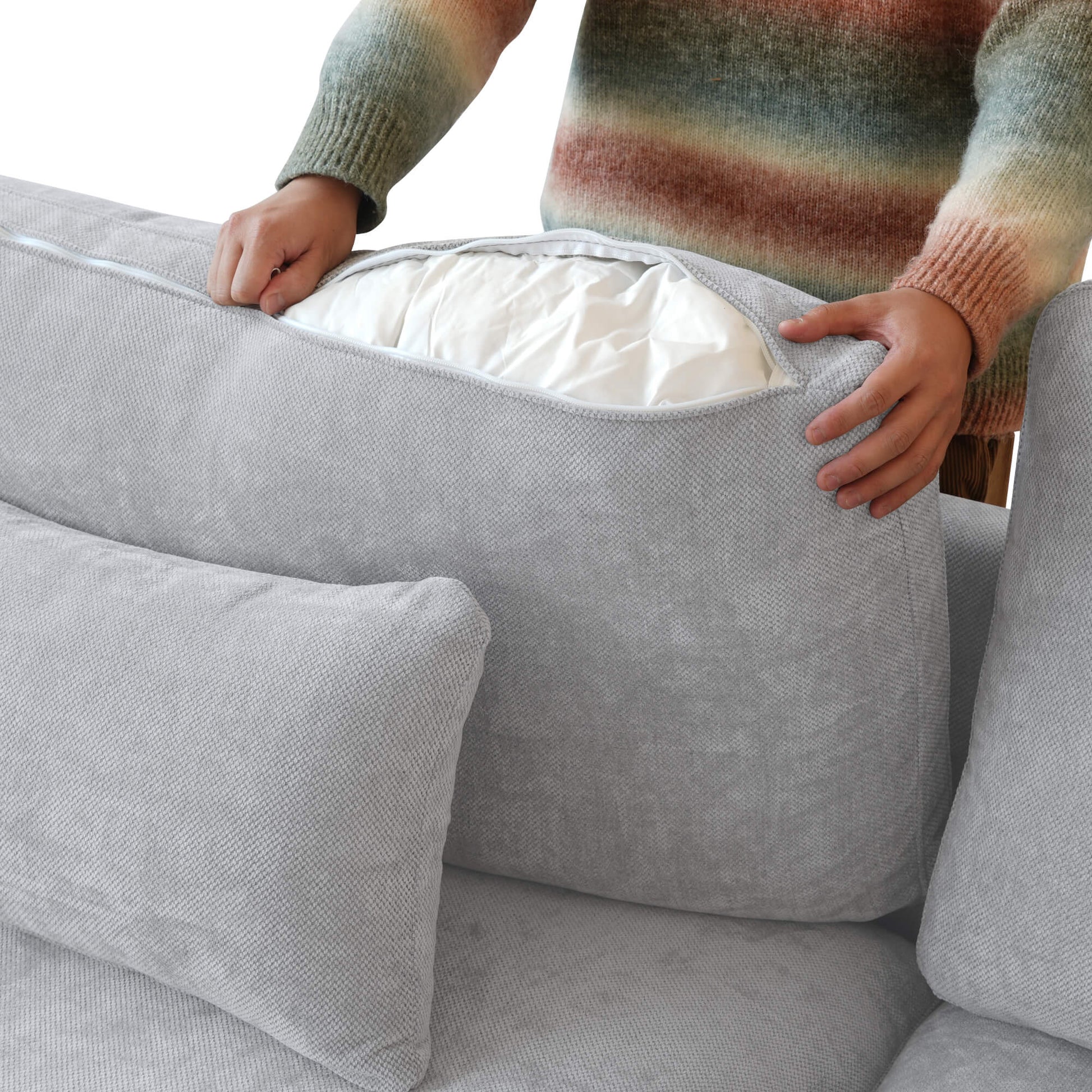 Person unzipping a linen cover of a backrest cushion of a gray sofa