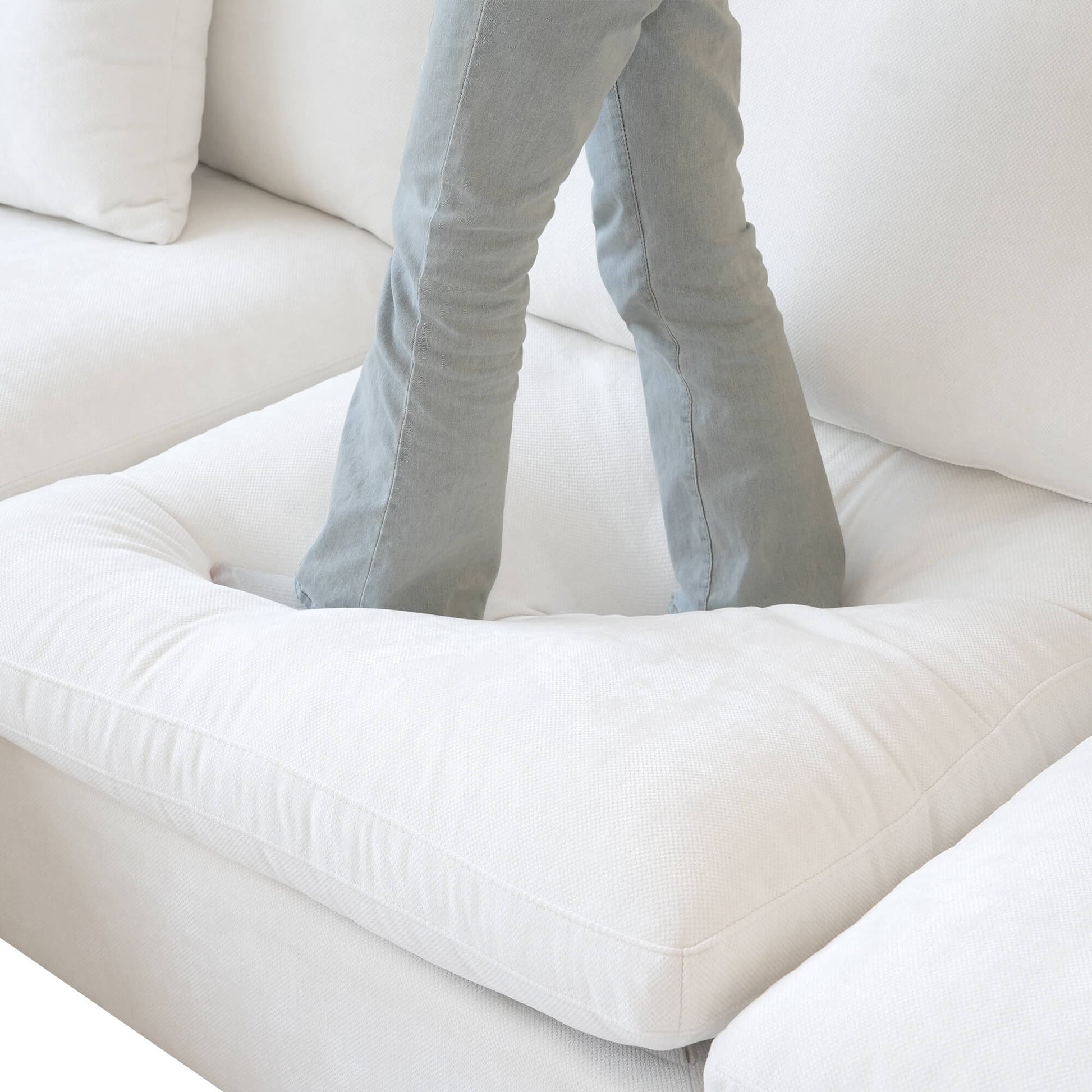 Person standing on a seat cushion of a white sofa to show its softness