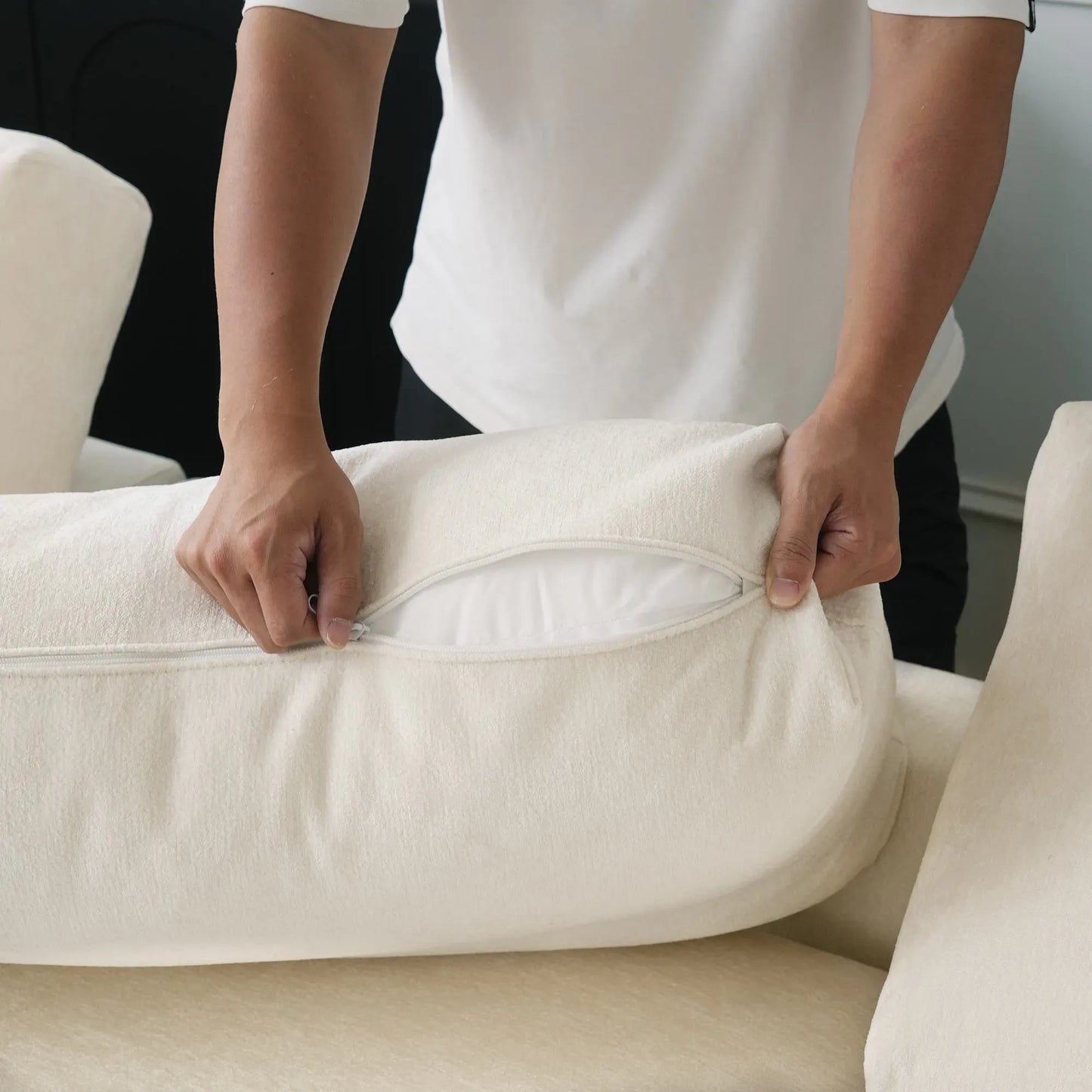 Person adjusting a beige pillow on a sofa