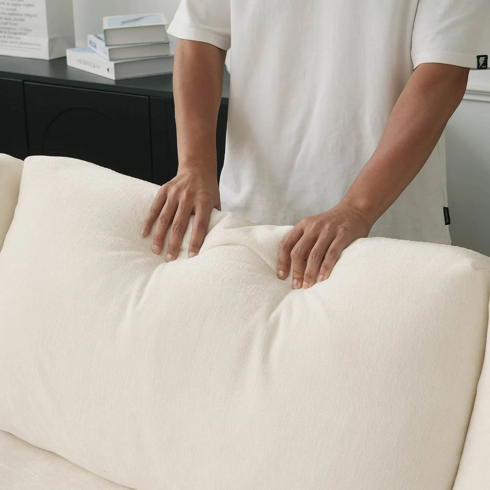Person adjusting a beige back cushion on a sofa