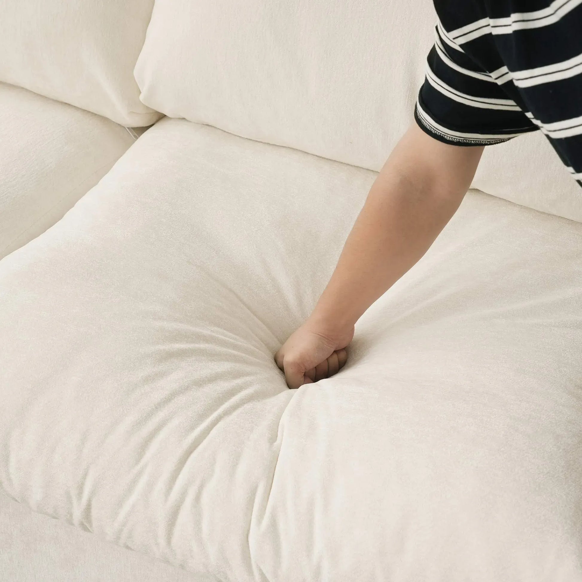 Person pressing on a seat cushion of a beige sofa