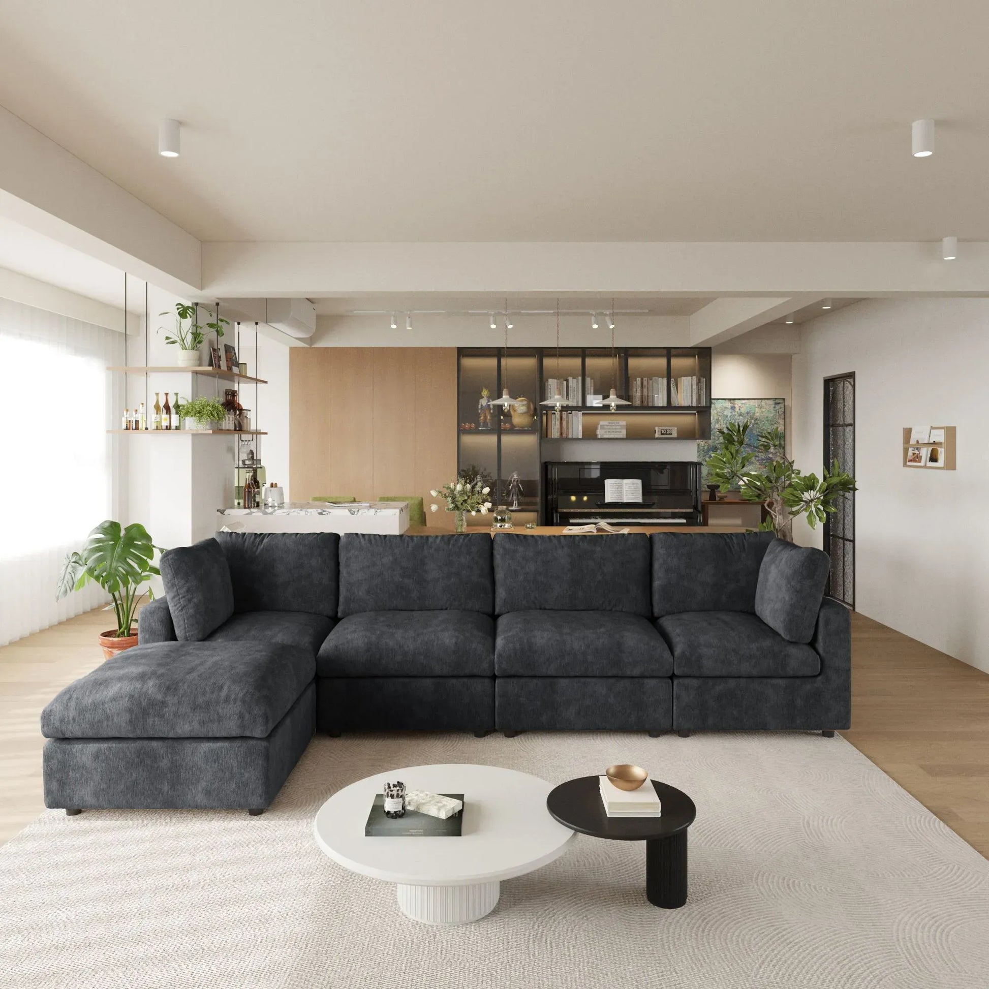 Modern living room with a black L-shaped 5-seater sectional sofa, coffee tables, and a kitchen in the background.
