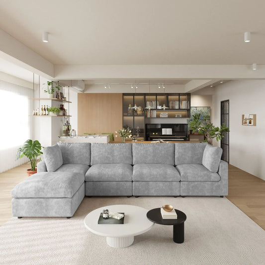 Modern living room with a gray L-shaped 5-seater sectional sofa, coffee table, and kitchen in the background.