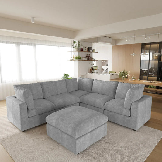 Gray V-shaped corner sectional sofa with ottoman in a modern living room with kitchen in the background
