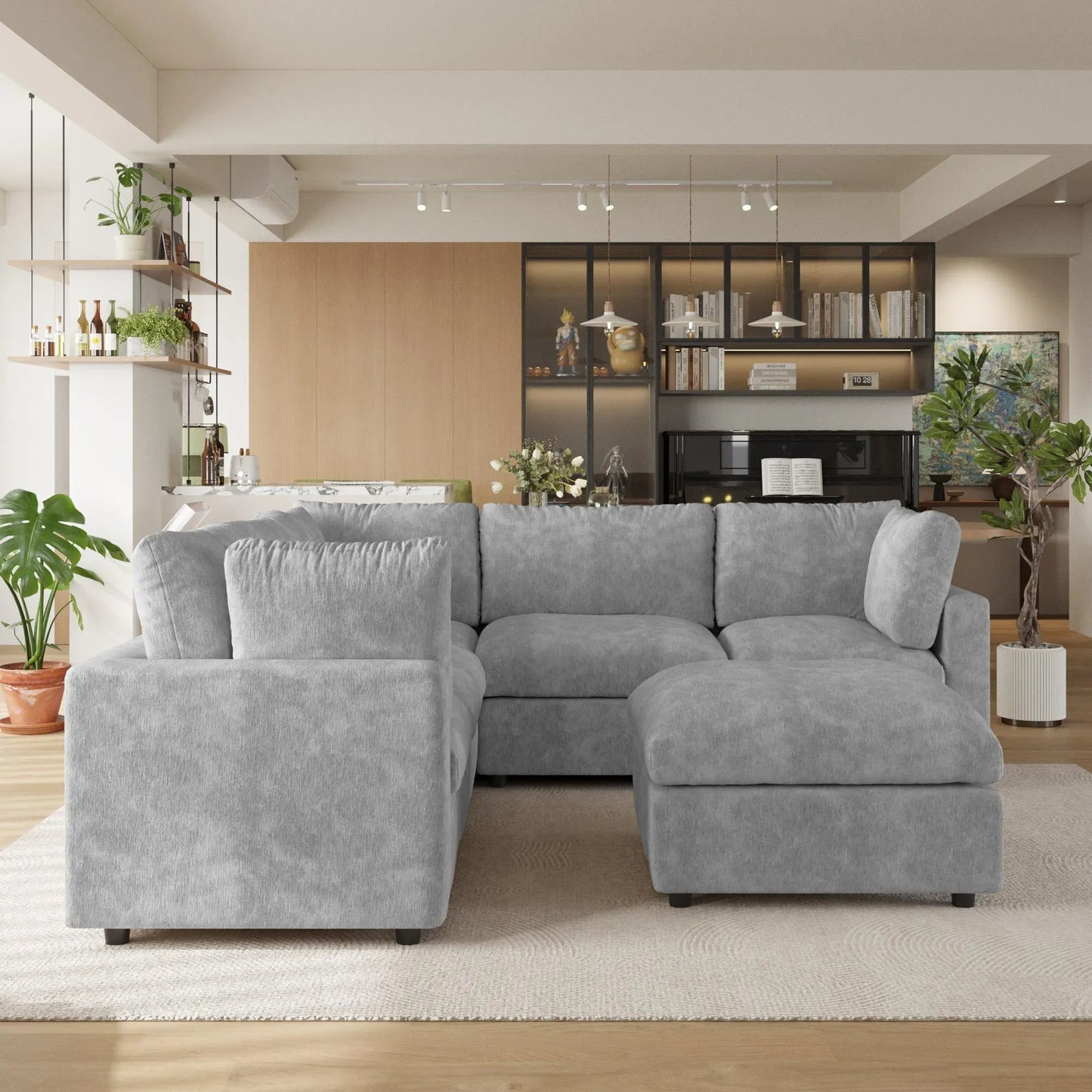 Gray V-shaped corner sectional sofa with ottoman in a modern living room with shelves and plants.