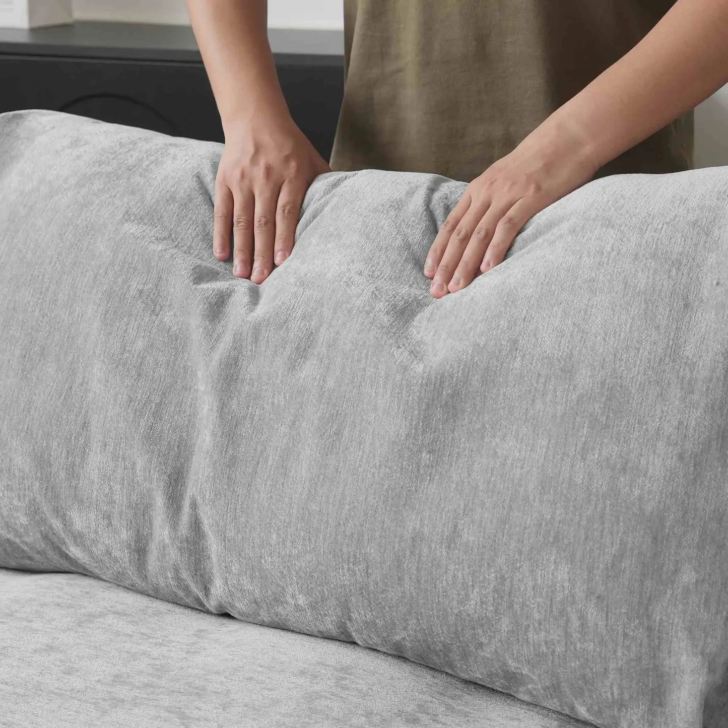 Person squishing a back cushion of a gray sofa to show its softness