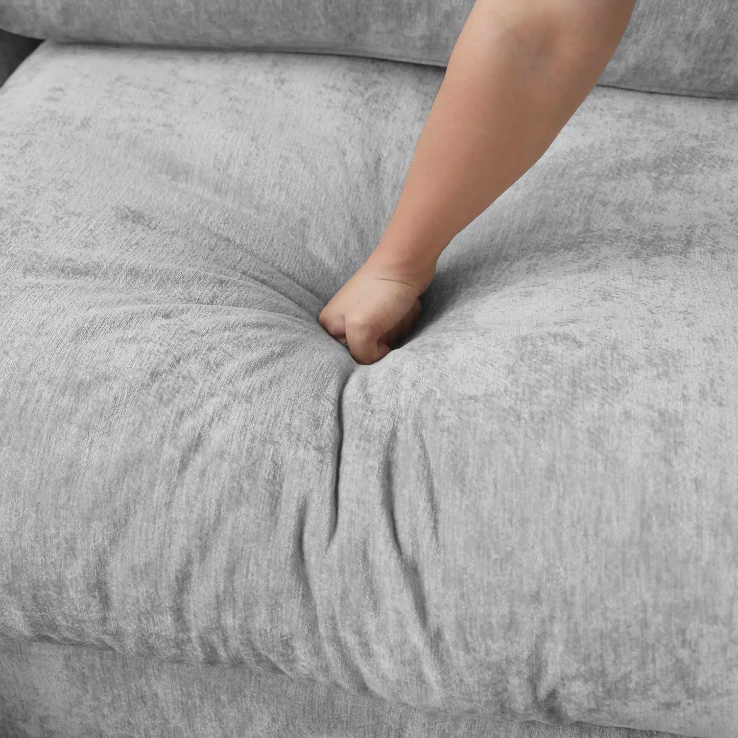 Close-up of a person pressing hand onto seat cushion of a gray sofa to show its sink-in comfort