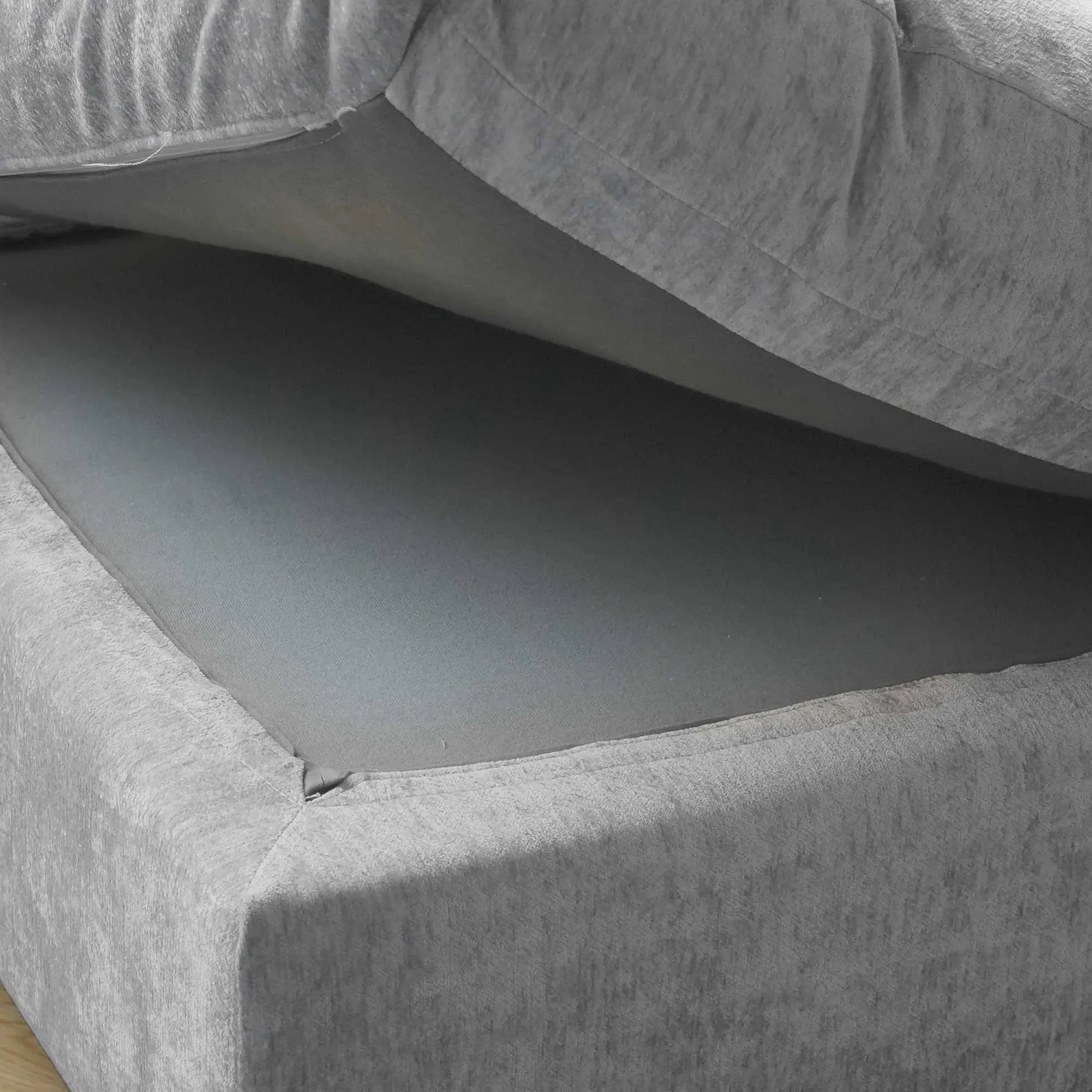 Close-up of a seat cushion of a gray sofa  being held up to show what's under it