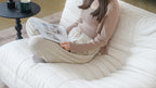 Person sitting on a white togo-style caterpillar sofa reading magazine. 