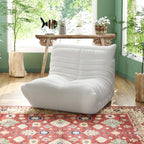 A distinctive white caterpillar-shaped floor sofa placed on a patterned rug in a room with green walls and a wooden table.