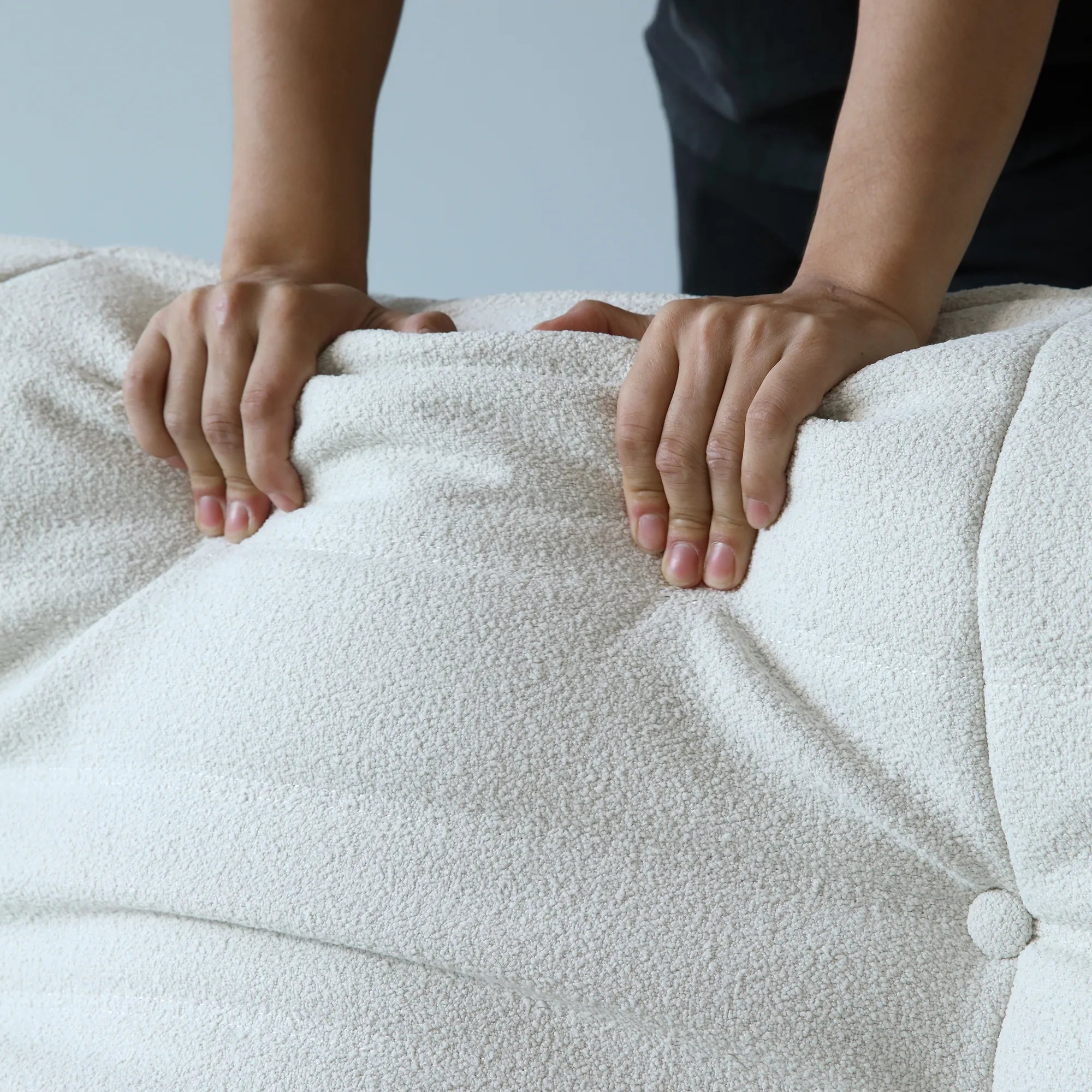 Person pressing on the back cushion of a white sofa to show its softness