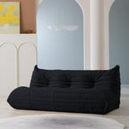 A black, caterpillar-shaped Togo sofa with a plush texture, situated in a room with minimalist decor.