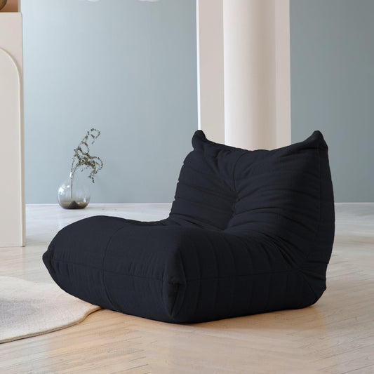 A distinctive black caterpillar-shaped floor armchair placed on a wooden floor in a room with light blue walls.