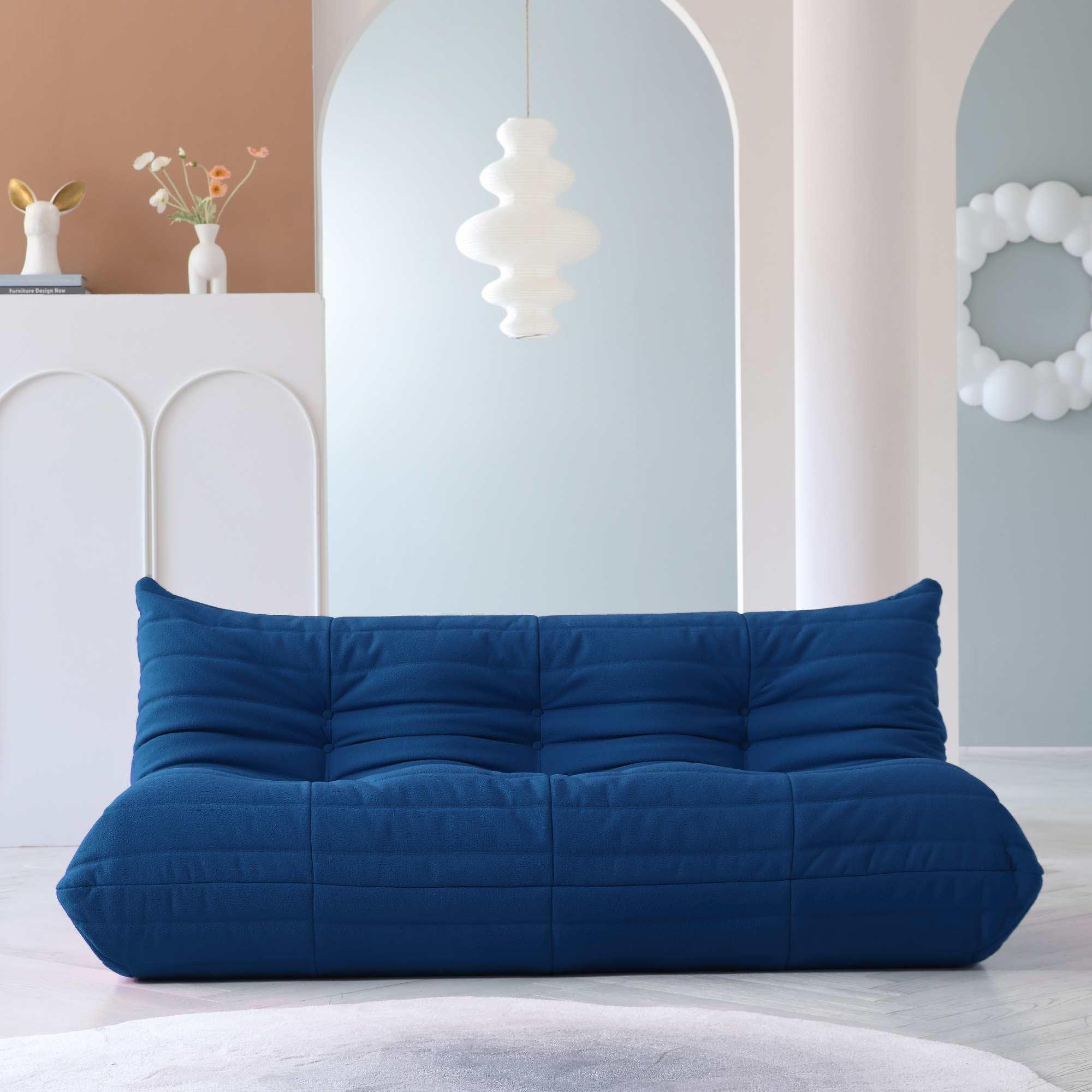 A distinctive blue caterpillar-shaped 3-seater Togo sofa placed on a white floor in a room with light-colored walls.