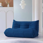 A blue, caterpillar-shaped Togo sofa on a wooden floor with a light blue wall in the background.