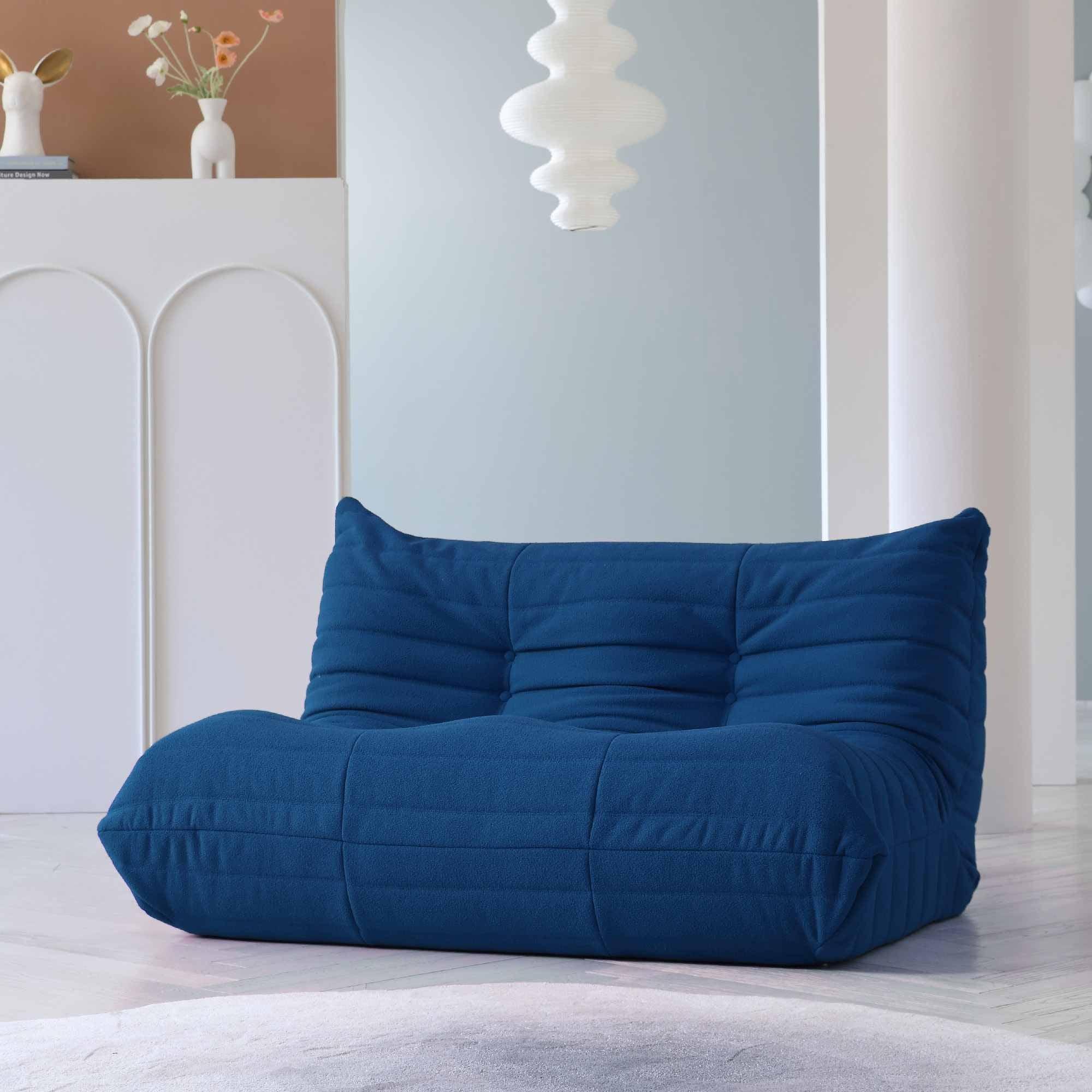 A blue, caterpillar-shaped Togo sofa on a wooden floor with a light blue wall in the background.