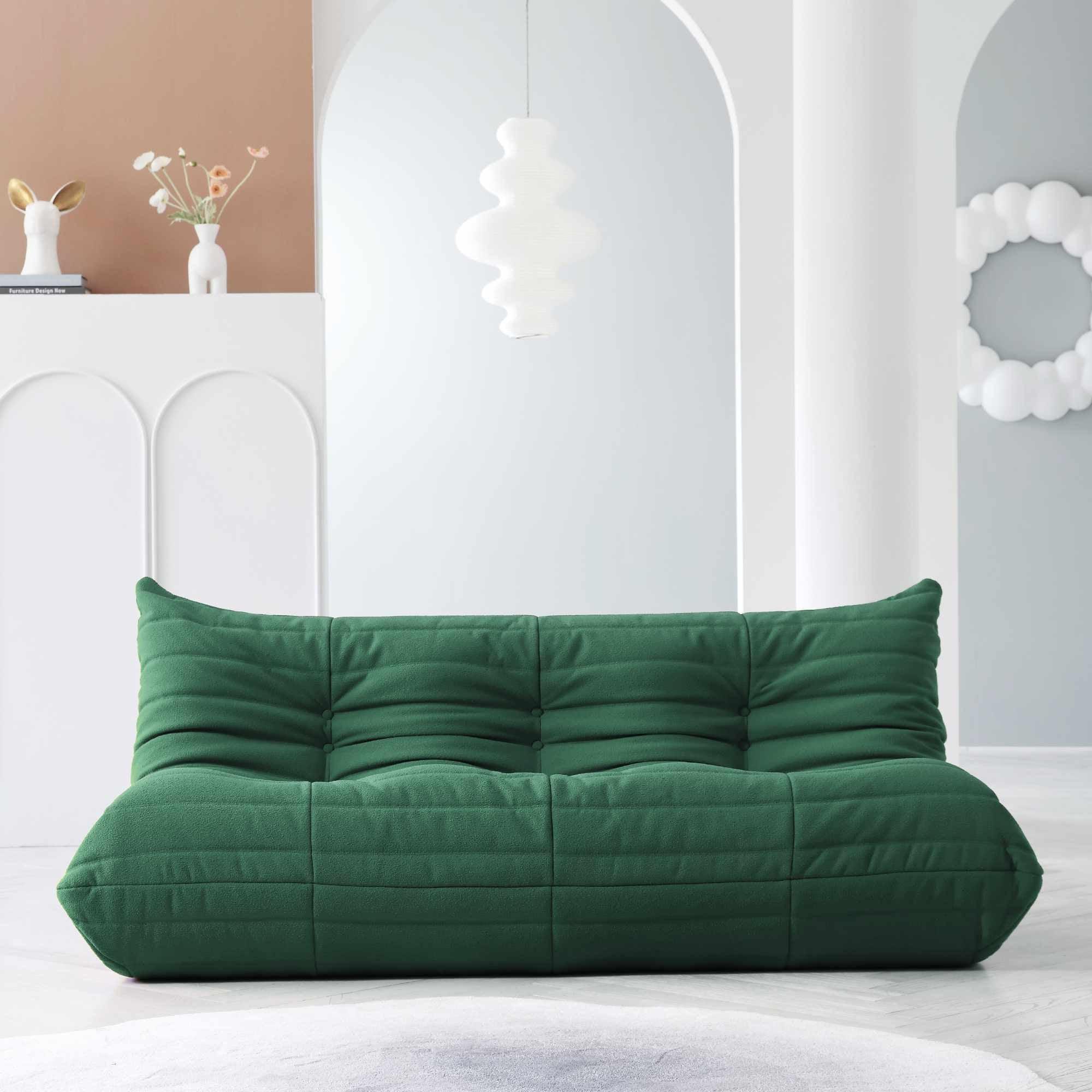 A distinctive green caterpillar-shaped 3-seater Togo sofa placed on a white floor in a room with light-colored walls and a painting in the background.