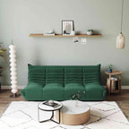 A green, caterpillar-shaped Togo sofa with a plush texture, situated in a room with minimalist decor, on a patterned rug.